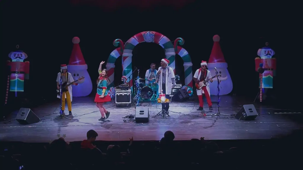 Escena del espectáculo infantil navideño "Mi Plan de Navidad" con músico en directo, luces de colores y ambiente familiar festivo